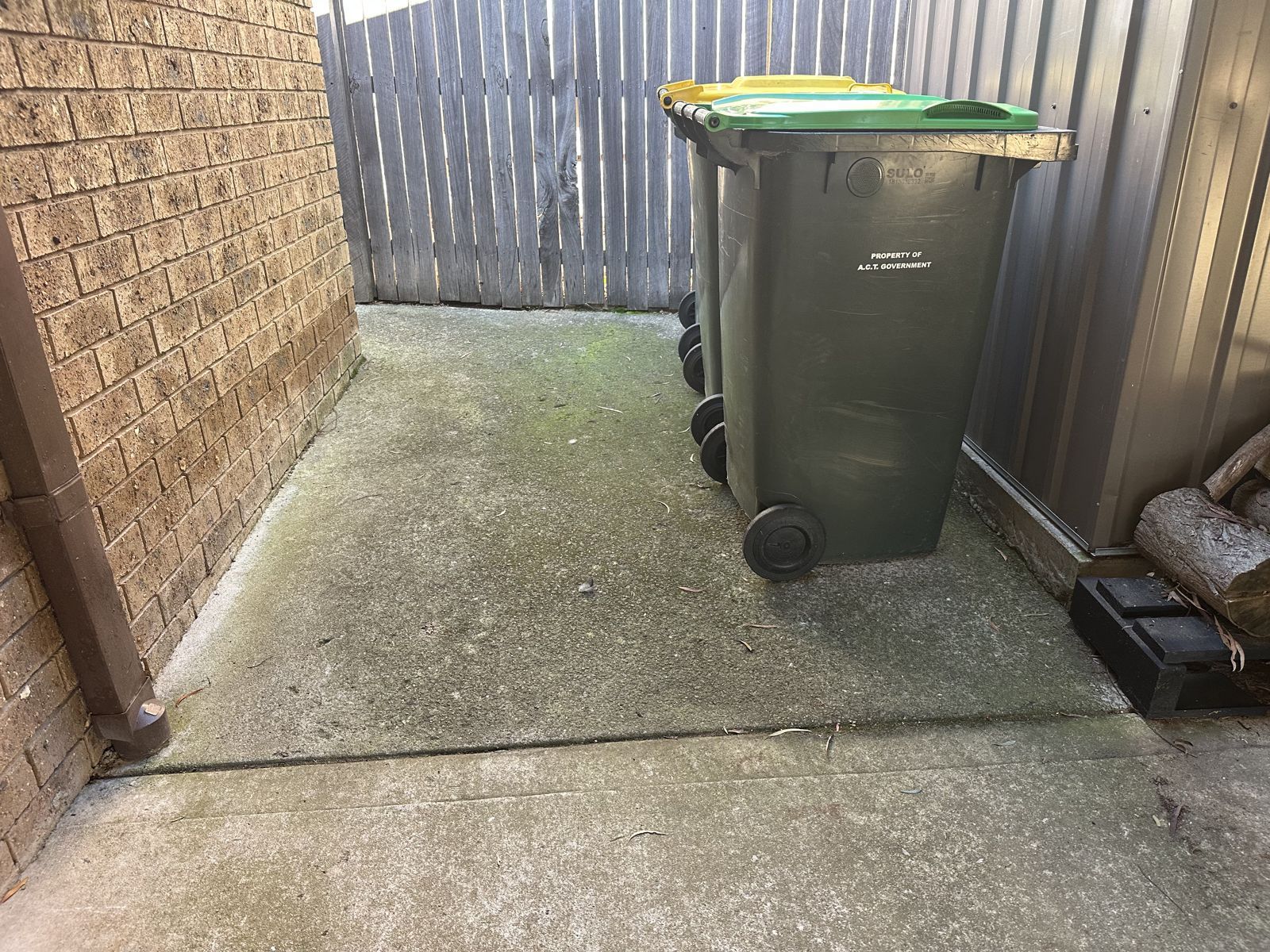 Algae-stained concrete bin area beside a Canberra home before pressure washing