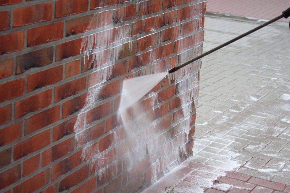 Soft wash cleaning solution applied to a brick house wall